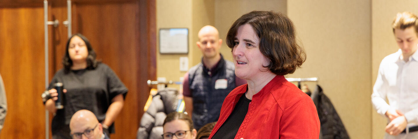 A woman stands speaking in a room of people