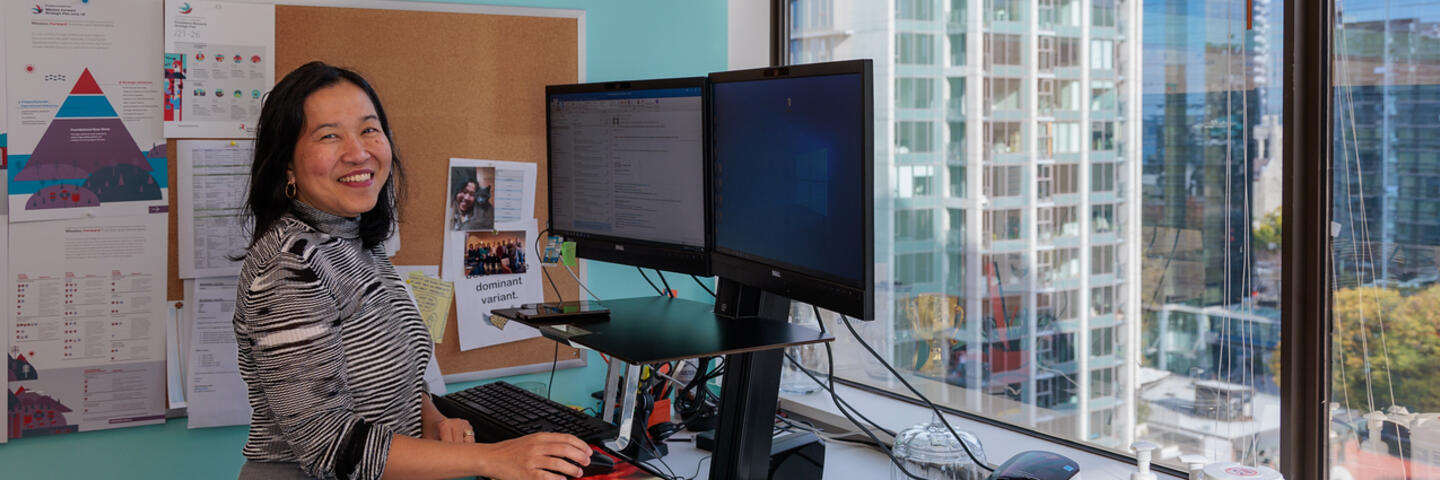 A smiling woman stands at a computer in an office