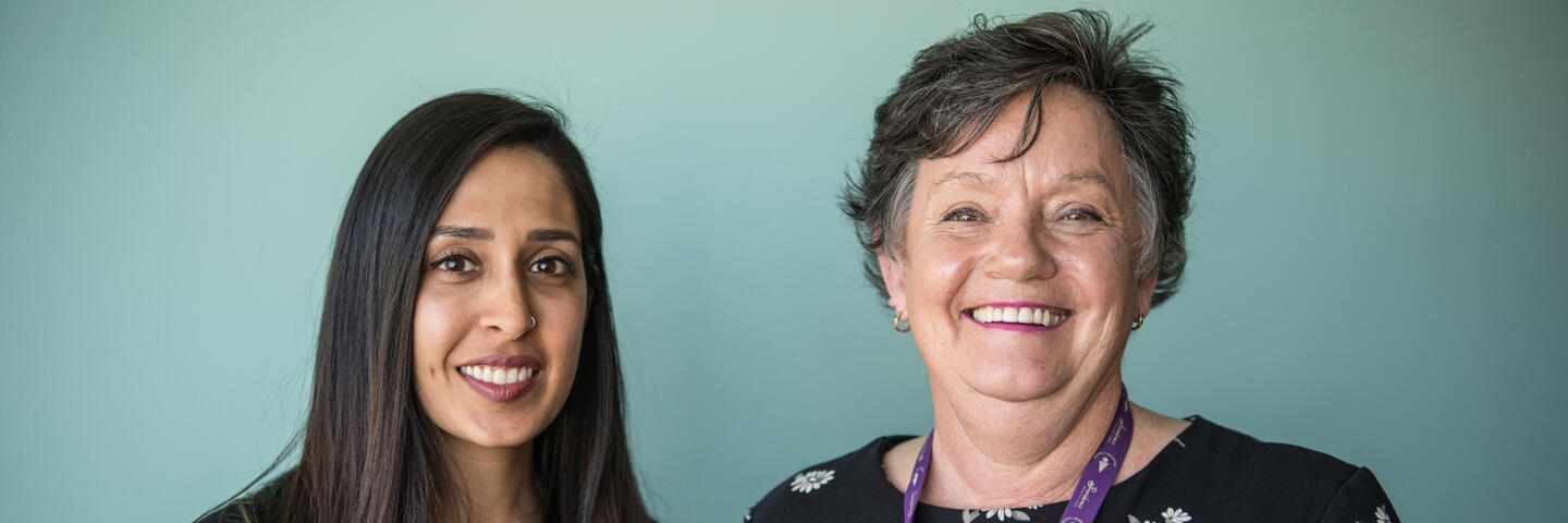 Two women stand in front of an office wall