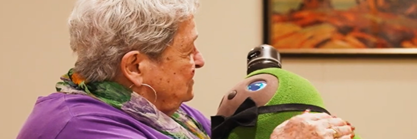 A woman holds Kiwi, a green plush robot