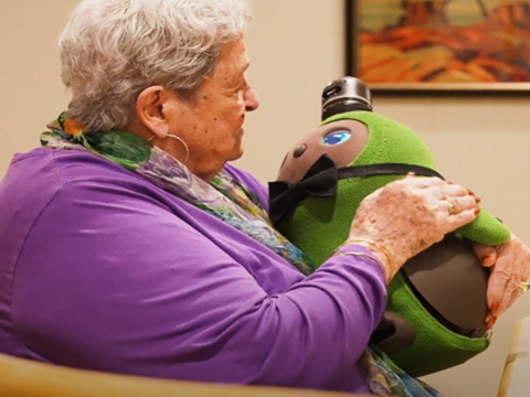 A woman holds Kiwi, a green plush robot